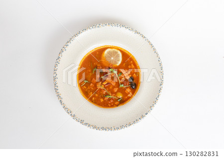Rich soup with smoked meats, sausages, lemon, and olives, viewed from above on a white background 130282831