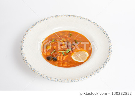 Rich soup with smoked meats, sausages, lemon, and olives on a white background 130282832