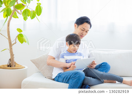 Family tablet dad and son relaxing on sofa 130282919