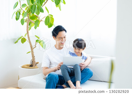 Family tablet dad and son relaxing on sofa 130282920