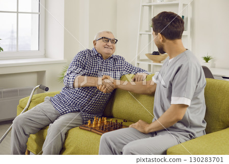Young nurse man playing chess game with smiling senior elderly at home. 130283701
