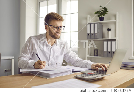 Young business man working at the desk with a pile of documents on his workplace at office. 130283739