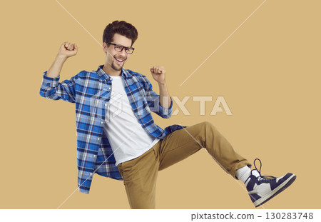 Cheerful funky hipster guy dancing rejoicing in success on beige background in studio. 130283748