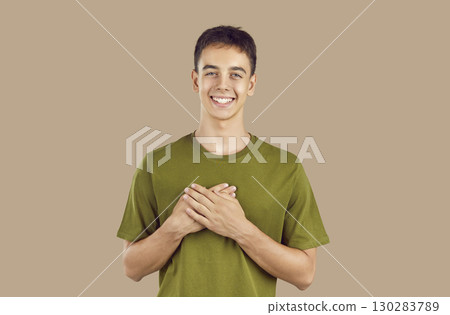 Portrait of touched positive teenage guy holding hands on chest expressing gratitude. 130283789