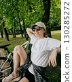 Young woman cyclist relaxing on park bench after an invigorating workout, soaking up fresh air and warm sunshine on beautiful summer day surrounded by nature. Female cyclist resting on park bench 130285272