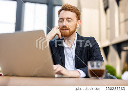 Confident focused man entrepreneur in suit working outdoors on computer 130285583