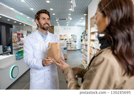 Dark-haired pretty young woman talking to the pharmacist and looking interested Dark-haired pretty young woman talking to the pharmacist and looking interested 130285695