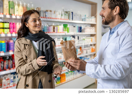 Dark-haired pretty young woman talking to the pharmacist and looking interested 130285697