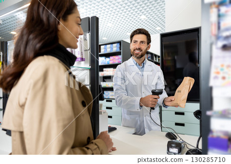 Pharmacist scanning barcode of the product while female client waiting for payment 130285710