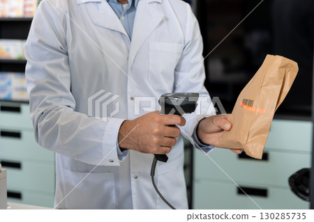 Pharmacist scanning barcode of the product while female client waiting for payment Pharmacist scanning barcode of the product while female client waiting for payment 130285735