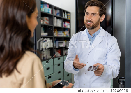 Male pharmacist offering pills to a female client 130286028