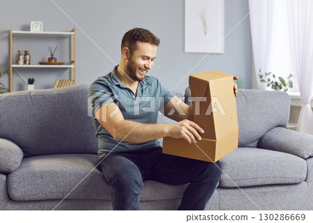 Happy man at home on the sofa opening a cardboard box, close-up 130286669