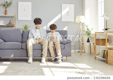 Boys Sitting on Sofa Playing Games on Phones 130286688