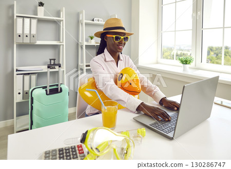 Funny woman sitting at the desk on workplace at office and booking tickets for summer vacation. 130286747
