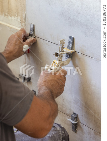 Craftsman using tile leveling system during tiling a wall, closeup. Construction or rennovation of a house Craftsman using tile leveling system during tiling a wall, closeup. Construction or rennovation of a house 130286773