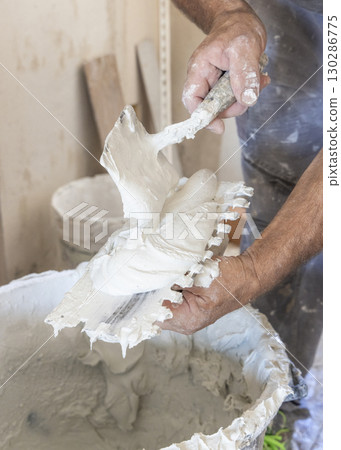 Craftsman spreads tile adhesive on notched trowel, dirty hands closeup. Construction process Craftsman spreads tile adhesive on notched trowel, dirty hands closeup. Construction process 130286775