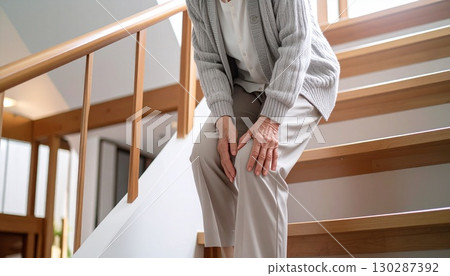 An elderly person slowly and carefully descends the stairs while rubbing his knee Image of knee pain and senior life 130287392