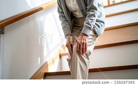 一位老人一邊揉著膝蓋，一邊緩慢而小心地走下樓梯。膝蓋疼痛與老年生活的圖片 130287393