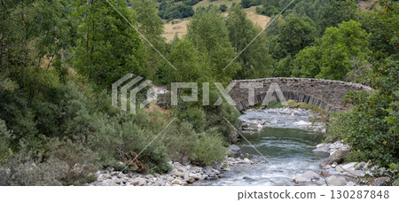Scenic view of Pyrenees stone bridge over Gavarnie stream at dawn, surrounded by lush greenery and Scenic view of Pyrenees stone bridge over Gavarnie stream at dawn, surrounded by lush greenery and 130287848