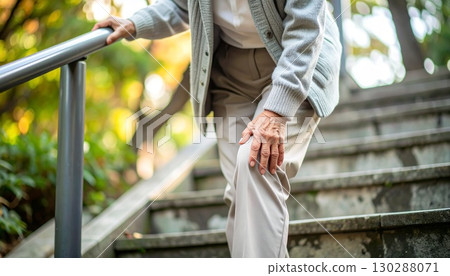 一位老人一邊揉著膝蓋,一邊緩慢而小心地走下樓梯。膝蓋疼痛與老年生活的圖片 一位老人一邊揉著膝蓋,一邊緩慢而小心地走下樓梯。膝蓋疼痛與老年生活的圖片 130288071