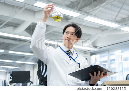 A young male researcher in a white coat conducting an experiment in a laboratory 130288135