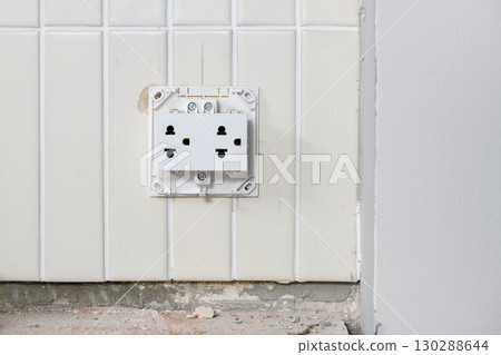 Close up detail of an exposed electrical outlet on tile wall during house renovation. construction site shows an unsafe power socket requiring repair and maintenance 130288644