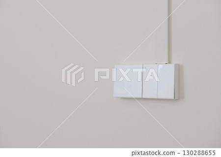 Minimalist detail of white light switch on plain wall part of house renovation. An essential element for home construction and electrical wiring in modern interior Minimalist detail of white light switch on plain wall part of house renovation. An essential element for home construction and electrical wiring in modern interior 130288655