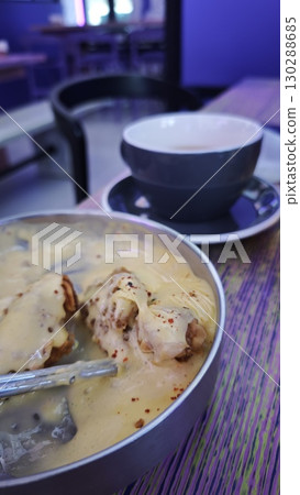 Korean fried chicken covered in melted cheese served in a metal bowl with a cup of hot drink in the background. The image captures indulgence, comfort food and urban dining culture 130288685