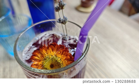 A glass of purple iced lemonade decorated with a vibrant edible flower and lavender sprigs. The image evokes freshness, creativity and botanical-inspired summer drinks A glass of purple iced lemonade decorated with a vibrant edible flower and lavender sprigs. The image evokes freshness, creativity and botanical-inspired summer drinks 130288688