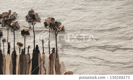 Dried flower arrangement with tall stems and textured petals on beige fabric background creating natural and rustic atmosphere 130289273