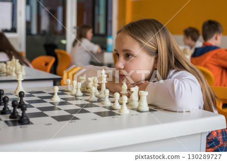 Concentrated schoolgirl playing chess game in school classroom. Child girl on chess lesson strategy 130289727