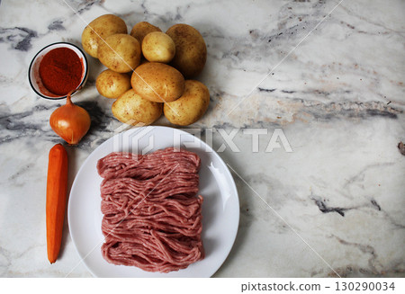 Potatoes, minced meat, paprika, seasoning, onions, carrots on the table. Potato recipe with meatballs cutlets 130290034