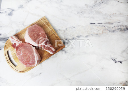 Two raw pork steaks lying on a wooden plank top view copyspace 130290059