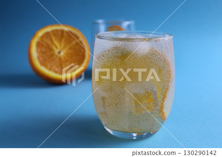 Step-by-step making of lemonade. Step 2. Pour the fruit orange with soda water. A glass of lemonade orange on a blue background with a place for text . close-up Step-by-step making of lemonade. Step 2. Pour the fruit orange with soda water. A glass of lemonade orange on a blue background with a place for text . close-up 130290142
