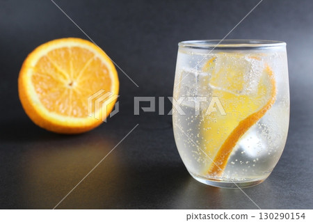 lemonade with orange and ice in a glass on a black background next to lies ice and orange. Summer drink on a black background 130290154