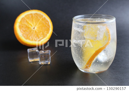 lemonade with orange and ice in a glass on a black background next to lies ice and orange. Summer drink on a black background 130290157