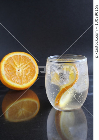 lemonade with orange and ice in a glass on a black background next to lies ice and orange. Summer drink on a black background 130290158