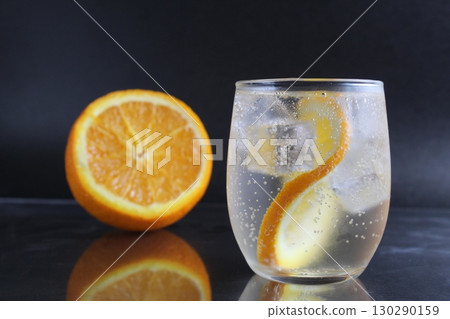 lemonade with orange and ice in a glass on a black background next to lies ice and orange. Summer drink on a black background 130290159