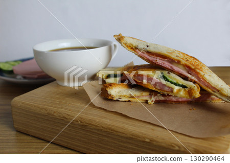 Breakfast on a tray of sandwiches with ham cheese greens on a wooden tray next to a cup of coffee tea. Breakfast to the room. Morning coffee 130290464