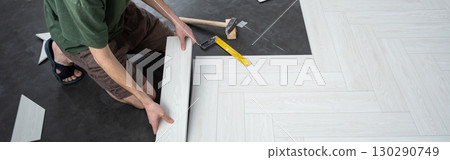 A man lays a quartz laminate on the floor. Renovation, Installation of French herringbone, banner A man lays a quartz laminate on the floor. Renovation, Installation of French herringbone, banner 130290749