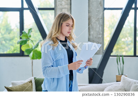 Serious young woman with business important papers standing in home interior 130290836
