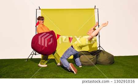 Man in orange shirt hits man in yellow shirt with giant red beanbag during playful fight Man in orange shirt hits man in yellow shirt with giant red beanbag during playful fight 130291016