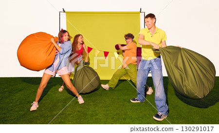 Group of young people playfully fighting with beanbags on green background Group of young people playfully fighting with beanbags on green background 130291017