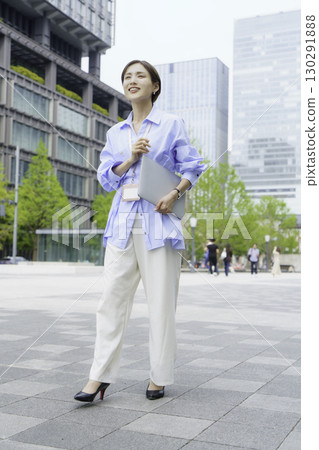 Portrait of a young businesswoman holding a laptop in an office district, vertical position Portrait of a young businesswoman holding a laptop in an office district, vertical position 130291888