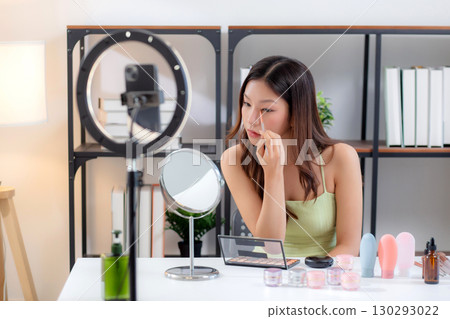 Asian woman applying makeup looking mirror while beauty tutorial, influencer lifestyle. 130293022