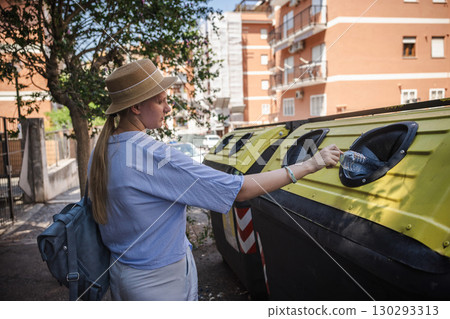 Young woman recycling a plastic bottle into a container on a city street on a sunny day 130293313
