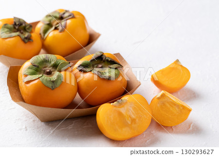 Fresh ripe persimmon in kraft paper bowl on white background, Autumn sweet fruit 130293627