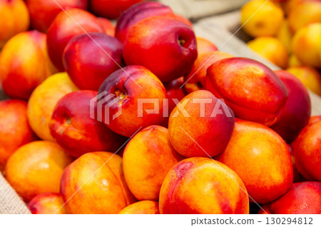 Close-up a lot of fresh red yellow colored peaches on market stall or in groceries shop area. Nectarines background. Fruit food background. Selective focus Close-up a lot of fresh red yellow colored peaches on market stall or in groceries shop area. Nectarines background. Fruit food background. Selective focus 130294812
