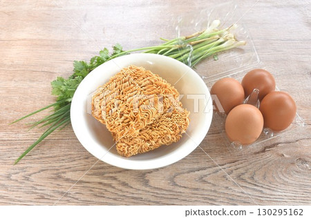 dry instant noodles on bowl with raw egg in plastic packaging and spring onion couple parsley prepare to cooking 130295162