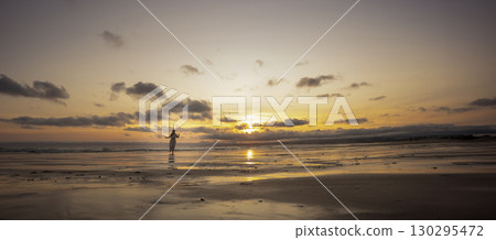 Woman walking on the beach at sunset with cloudy sky 130295472
